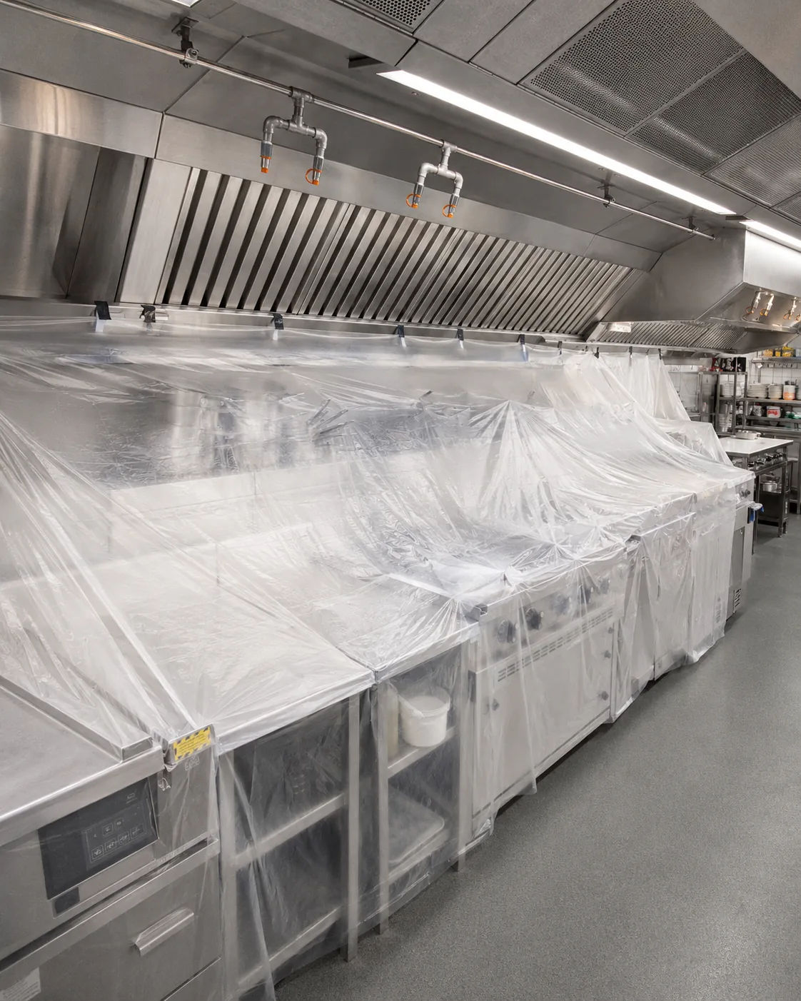 Technician draping protective plastic sheeting from the hood over the cooking line beneath a commercial kitchen exhaust hood before cleaning begins